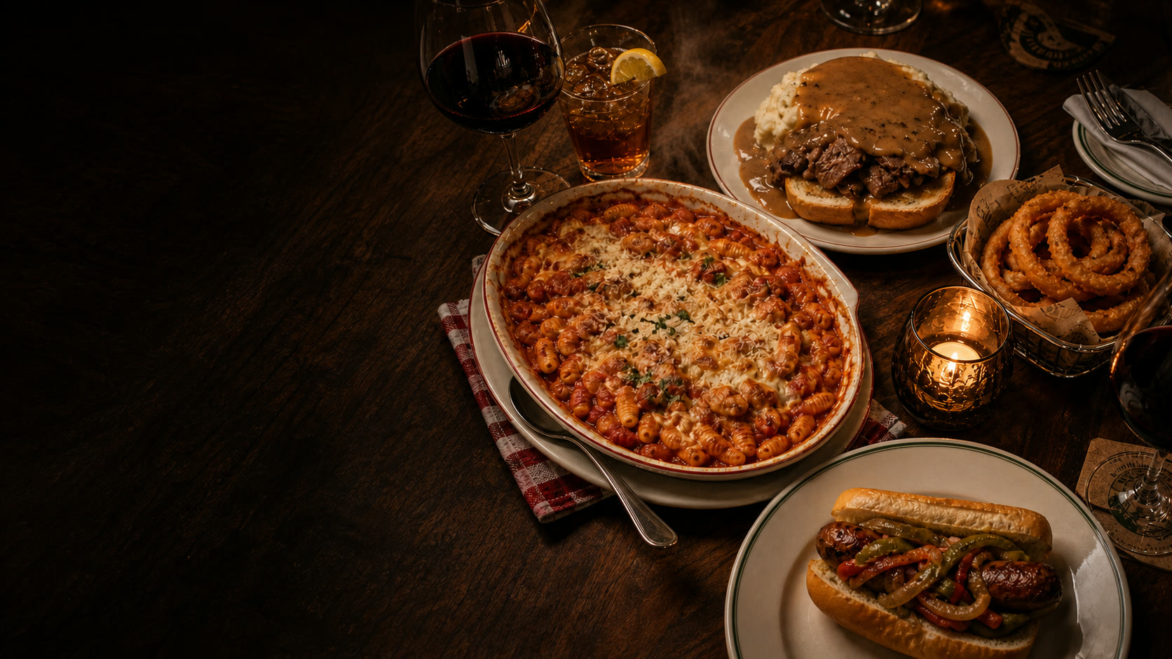 Supper-club table with baked cavatelli, hot beef sandwich, onion rings, and a Graziano sausage sandwich by candlelight